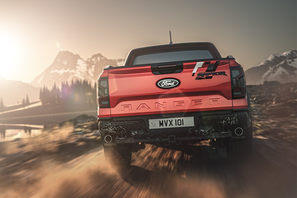 Vista trasera de un Ford Ranger Raptor circulando por un camino de tierra, con un paisaje montañoso de fondo.