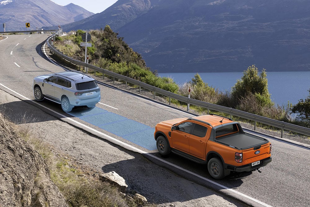 Imagen de un Ford Ranger Raptor amarilla circulando por un pintoresco camino de montaña, en la que se destacan los sistemas de asistencia al conductor del vehículo.