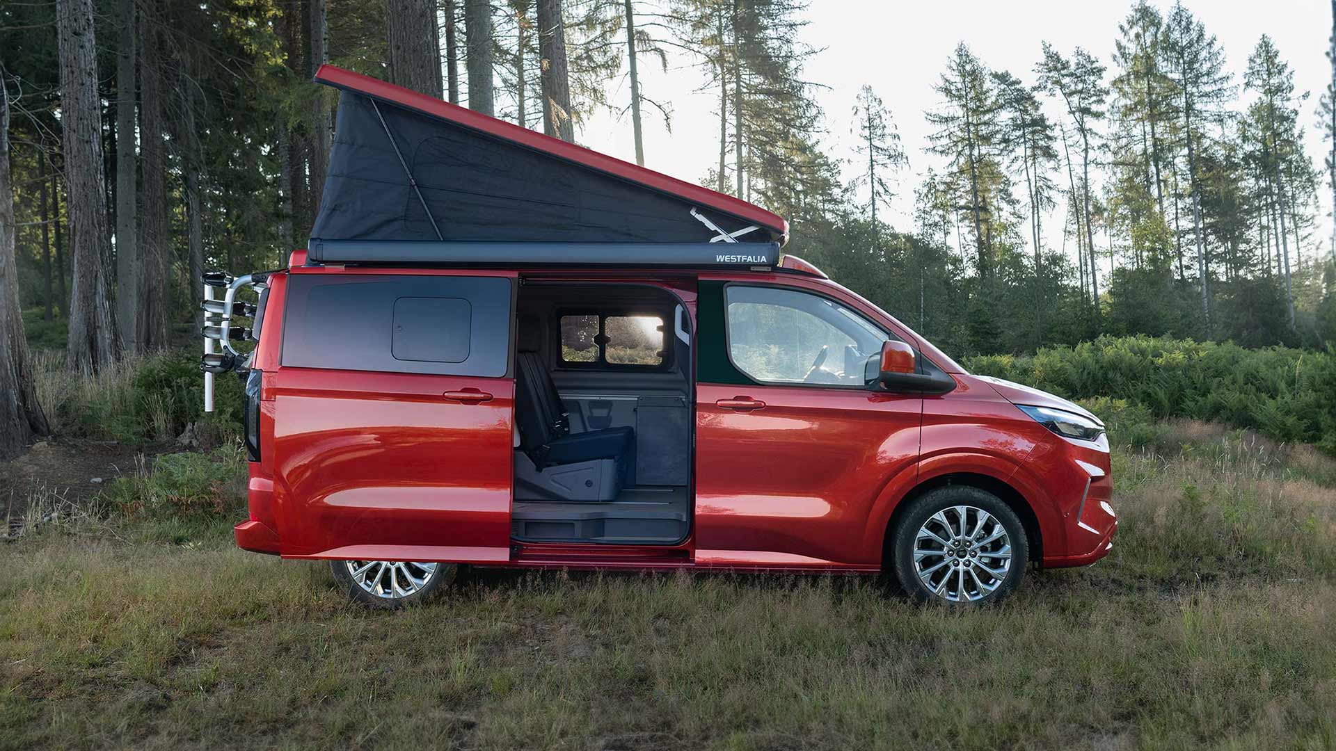 Ford Transit Custom Nugget roja aparcada con el techo con tejido autoplegable inclinado hacia arriba y la puerta lateral deslizante abierta.