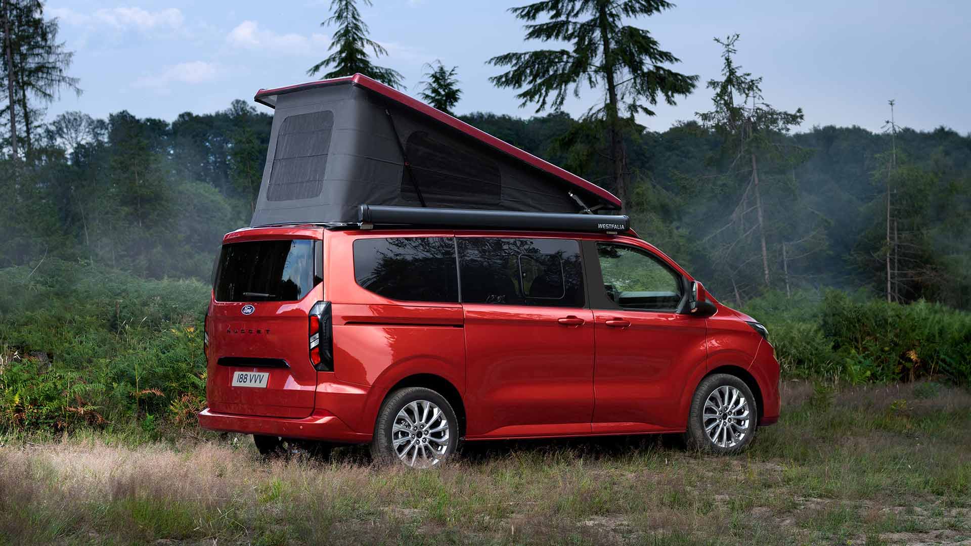 Ford Transit Custom Nugget roja aparcada en un campo de hierba, con el techo con tejido autoplegable inclinado hacia arriba.