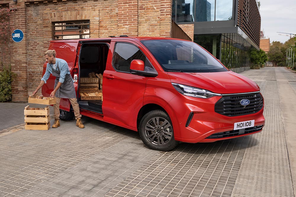 Conductor de una empresa de reparto cargando los paquetes en una Ford Transit Custom roja.