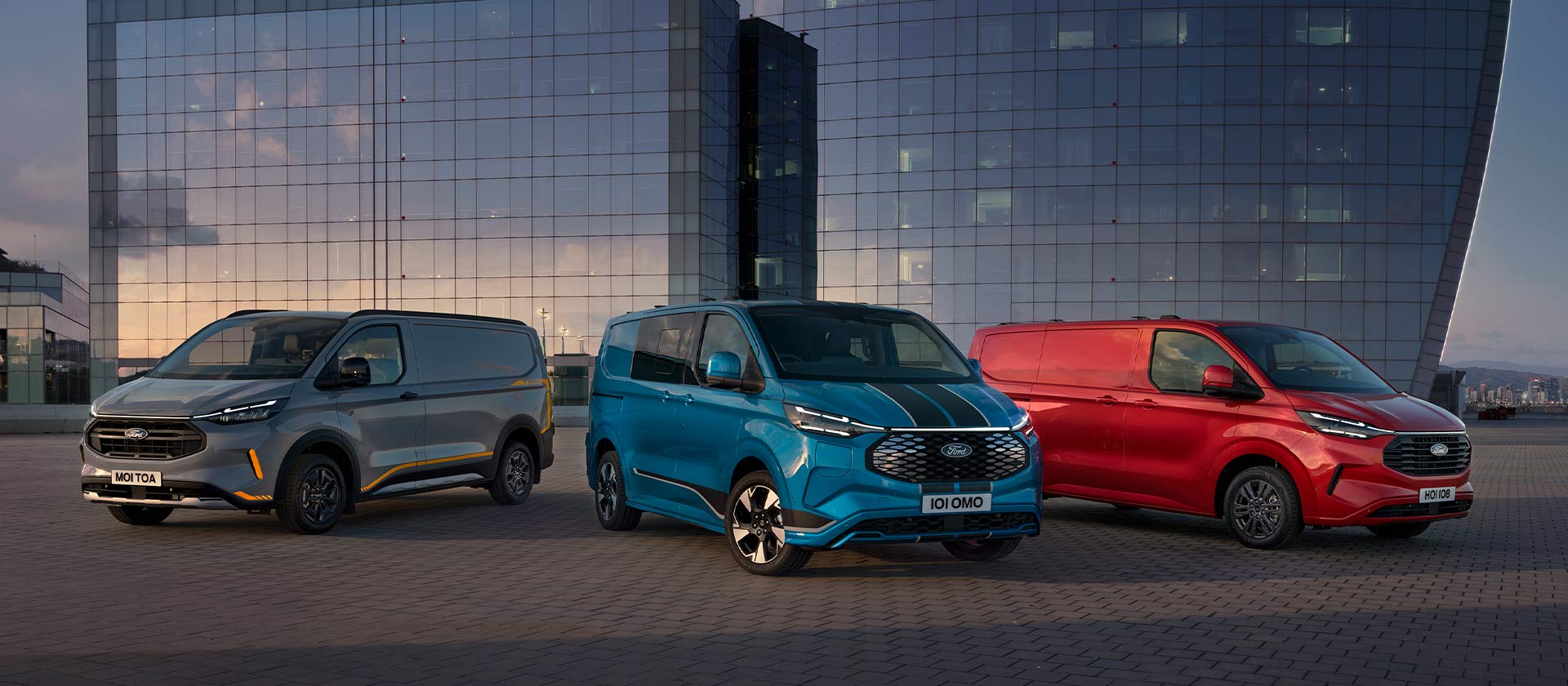 Tres furgonetas Ford Transit Custom Sport en gris, azul y rojo estacionadas. 