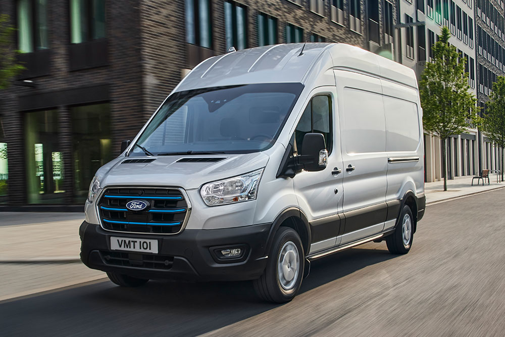 Furgoneta Ford E-Transit plateada circulando por una vía urbana.