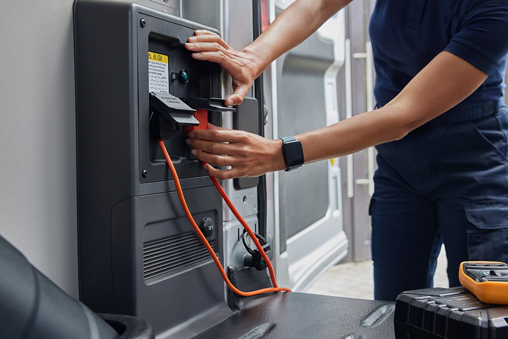 Primer plano de una persona enchufando un cable de carga en una furgoneta eléctrica Ford E-Transit.