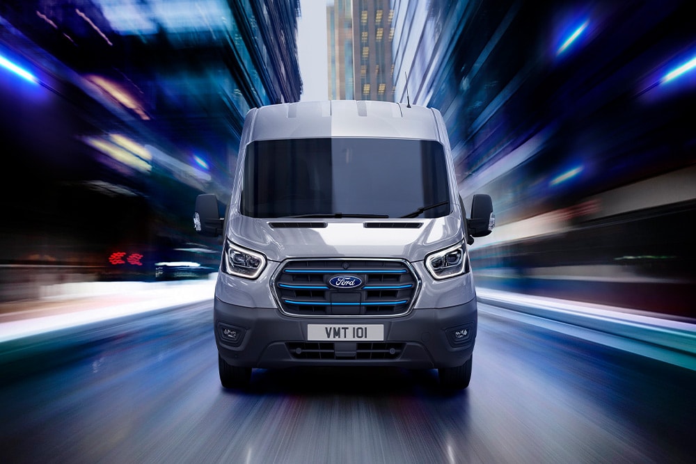 Vista delantera de dos furgonetas Ford Transit estacionadas en un garaje desde el que se ve la línea del horizonte de una ciudad a través de las ventanas.