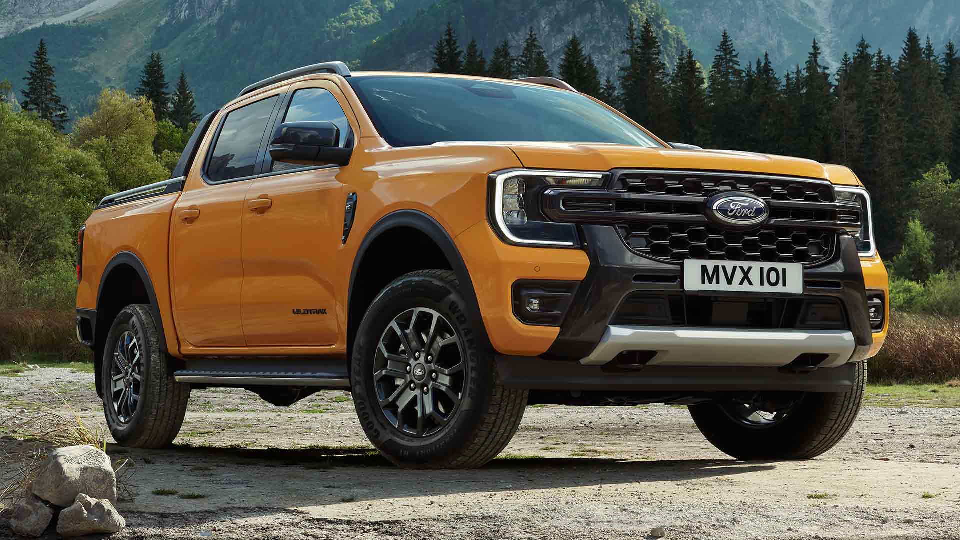 Un Ford Ranger Wildtrak con doble cabina amarillo con un pintoresco fondo boscoso y montañoso.