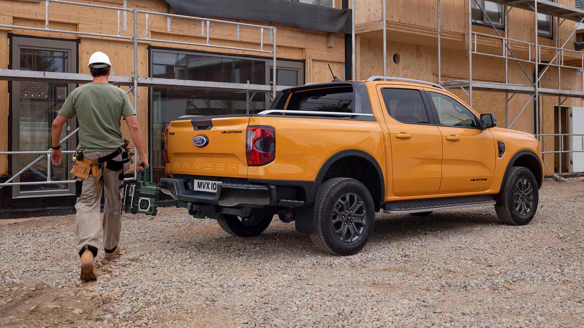 Vista trasera con plano tres cuartos de un Ford Ranger Wildtrak amarillo con cabina doble en una parcela de construcción.