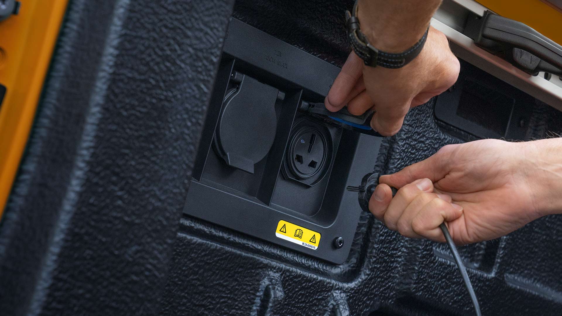 Primer plano de unas manos que conectan los cables a la toma de corriente en la caja de carga de un Ford Ranger.