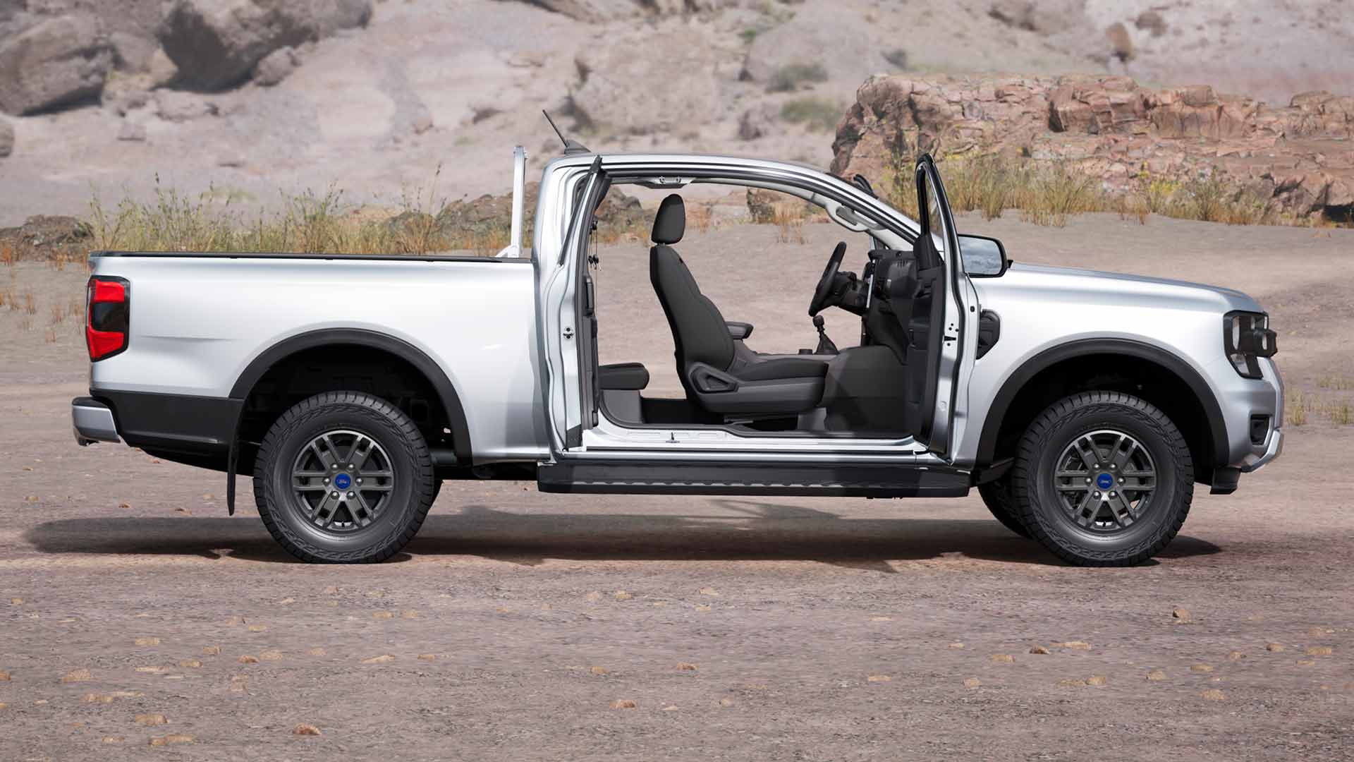Perfil de un Ford Ranger XLT Super Cab plateado con las puertas abiertas, estacionado en un terreno polvoriento.