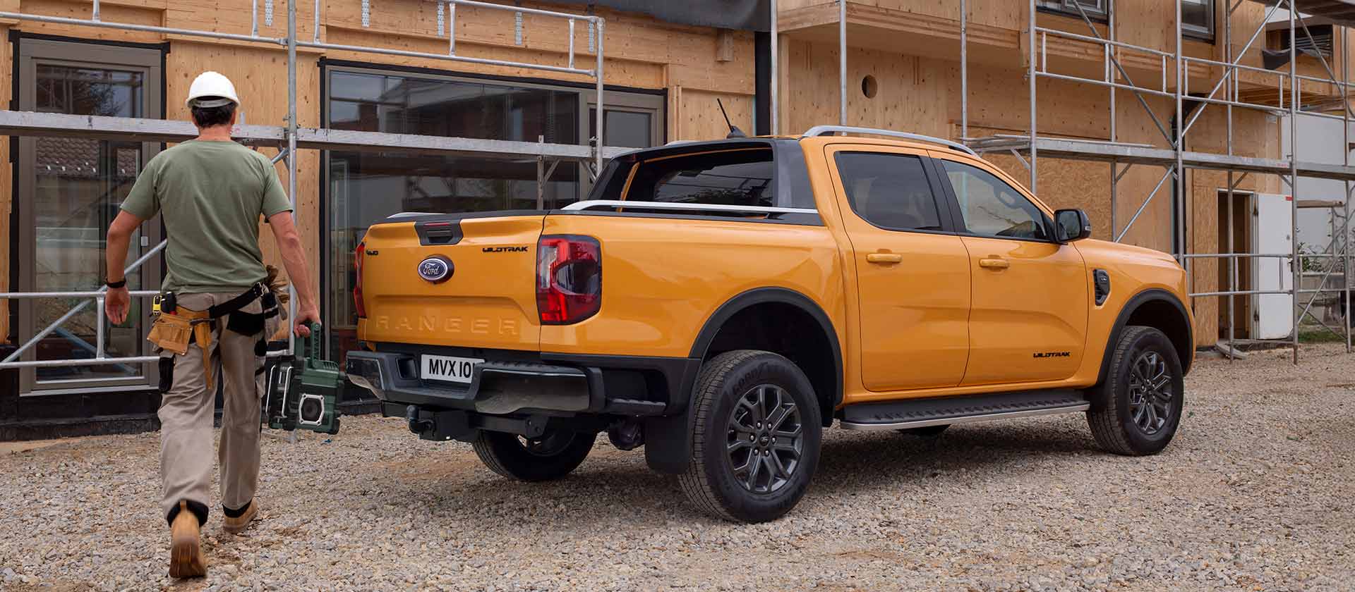 Vista trasera con plano tres cuartos de un Ford Ranger Wildtrak amarillo con cabina doble en una parcela de construcción.