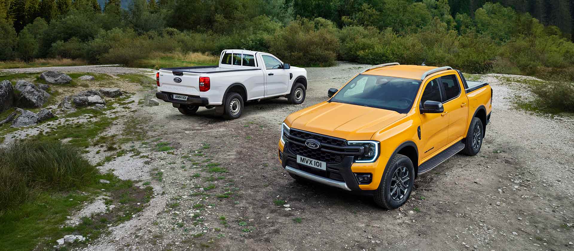 Un Ford Ranger blanco y un Ford Ranger amarillo estacionados a un lado de una carretera rocosa. 