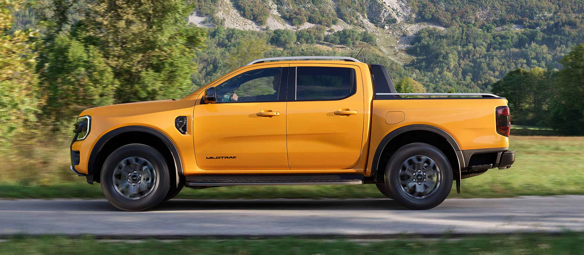 Vista lateral de un Ford Ranger Wildtrak amarillo recorriendo una carretera asfaltada.