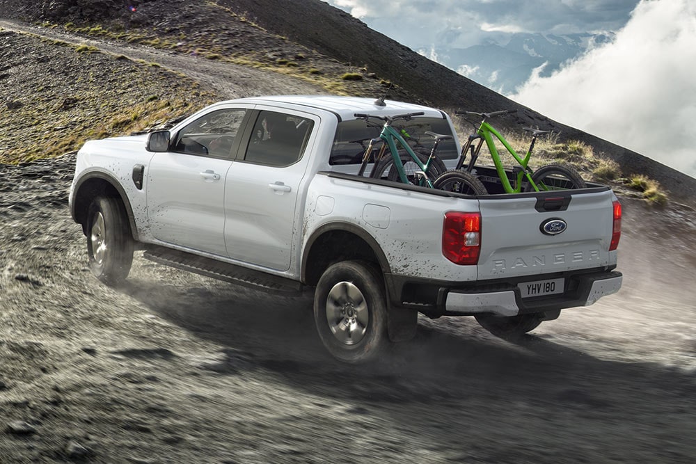 Un Ford Ranger híbrido enchufable Stormtrack sale de la carretera y sube una colina con dos bicicletas en el espacio de carga.