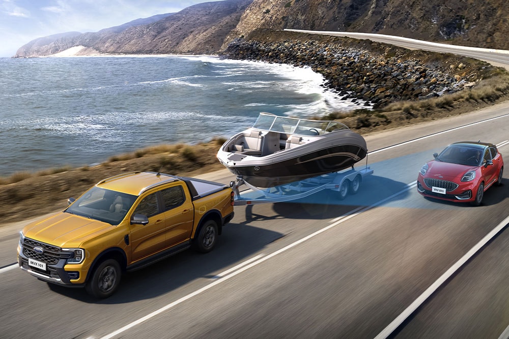 Un Ford Ranger amarillo remolca un barco mientras recorre una carretera costera, demostrando así su gran capacidad.