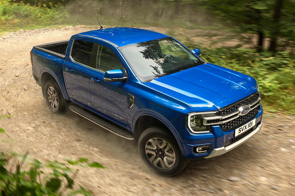 Un modelo pick-up Ford Ranger azul recorre un camino de tierra a través de un bosque, dejando un rastro de polvo.