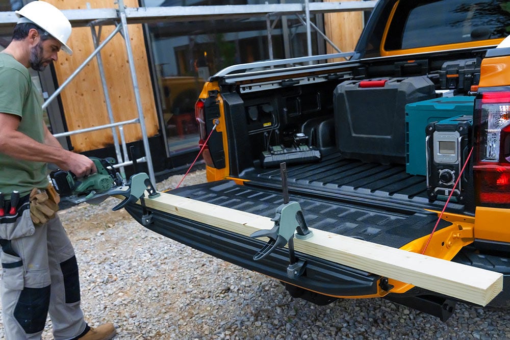 Se muestra el portón trasero de un Ford Ranger amarillo bajado con un tablón de madera asegurado con una abrazadera.