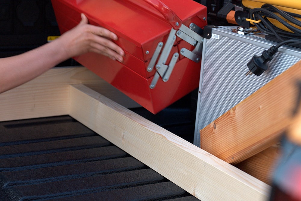 Primer plano de una mano dejando una caja de herramientas roja en la caja de carga de un Ford Ranger.