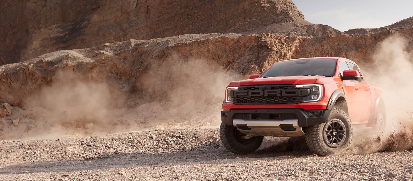 Un Ford Ranger Raptor rojo levanta polvo mientras recorre un paisaje desértico.