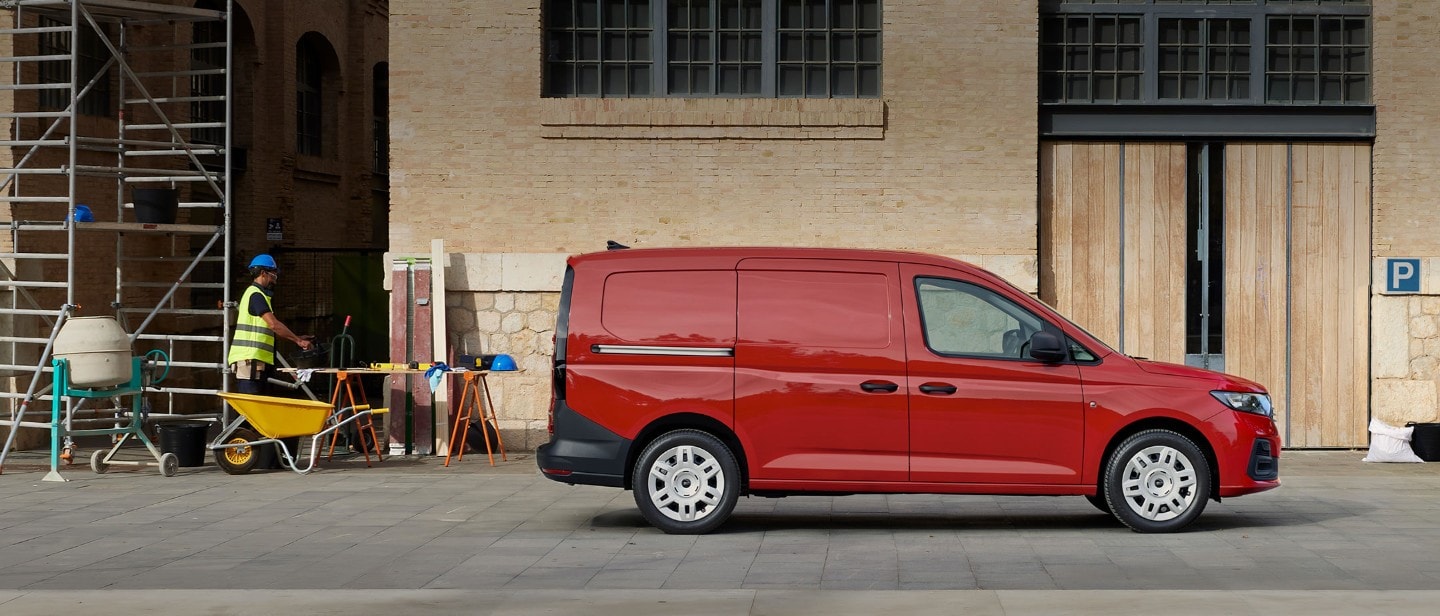 La nueva Ford Transit Connect en rojo arce estacionada en una obra de construcción muestra una puerta de carga lateral.