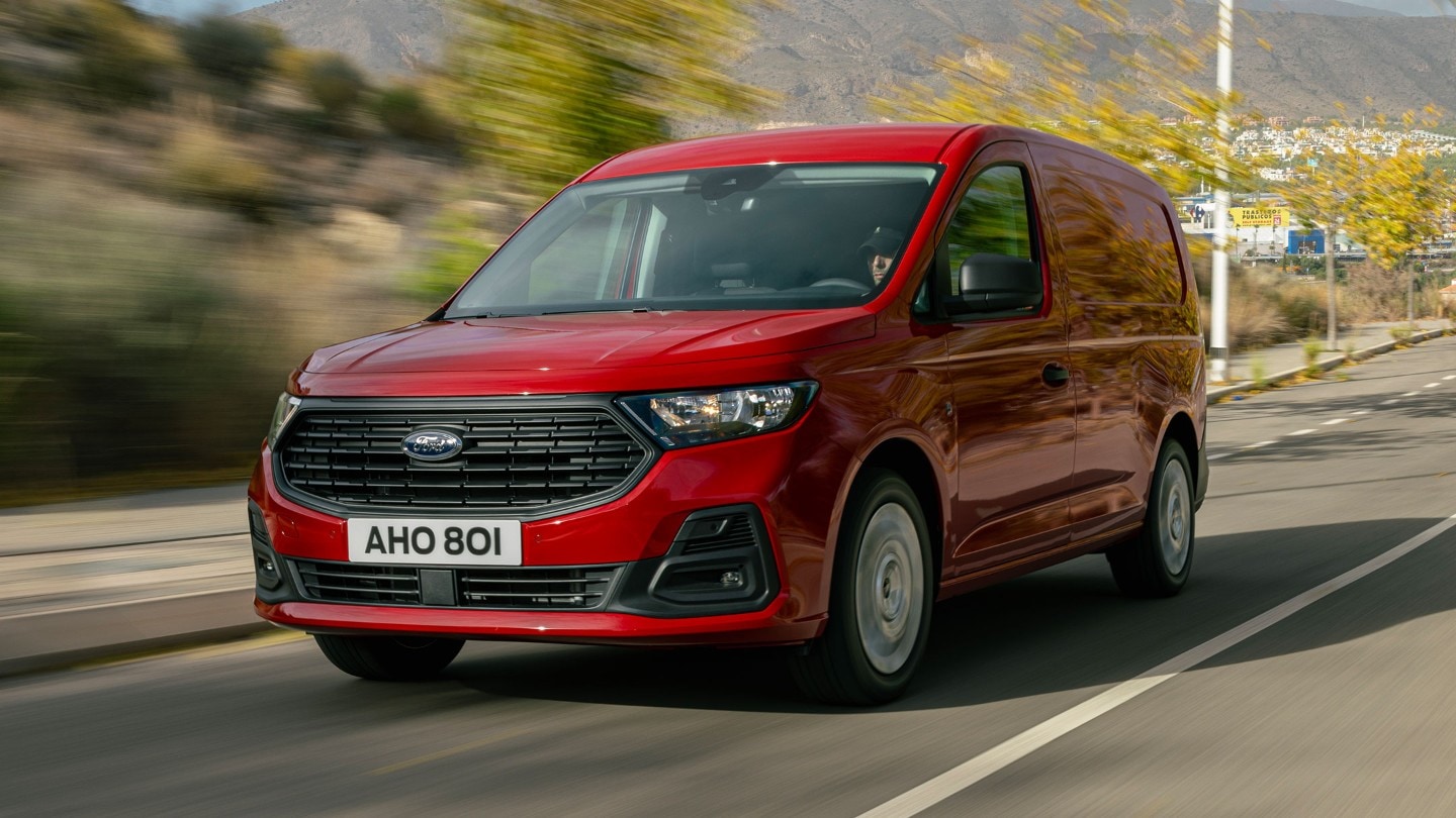 La nueva Ford Transit Connect en color rojo arce circula por una carretera con parrilla delantera y faros delanteros. 