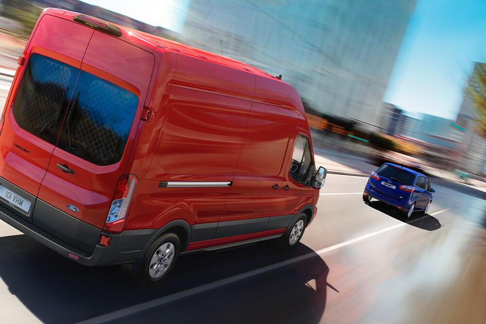 Una Furgoneta Ford Transit roja recorre una carretera urbana. 