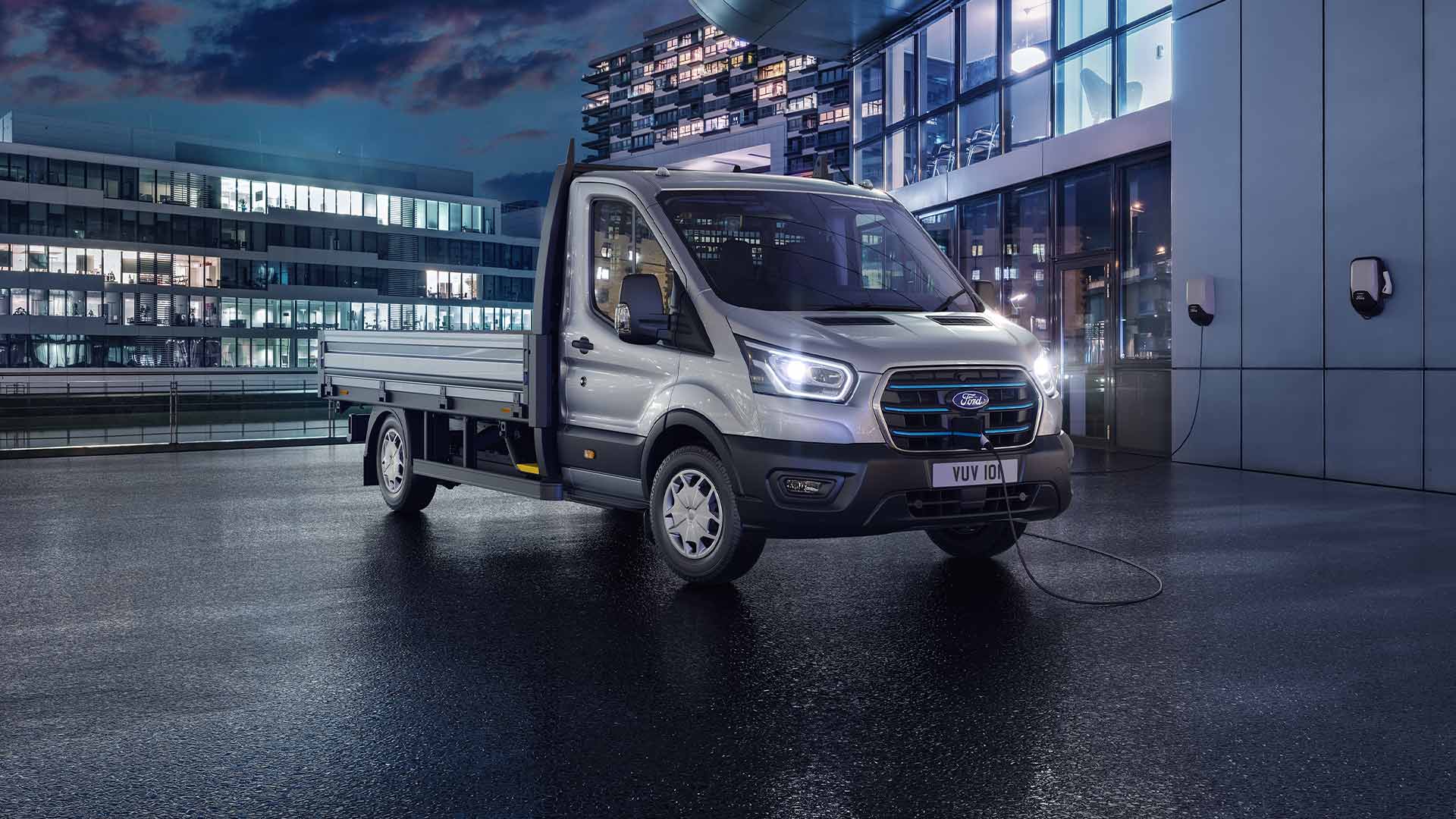 Una Ford Transit Chasis Cabina plateada estacionada frente a un edificio moderno por la noche.