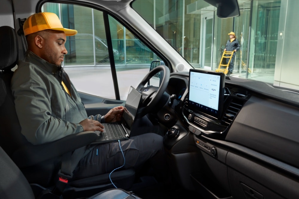 Imagen de un hombre sentado en el asiento del conductor de una furgoneta Ford Transit usando un ordenador portátil.