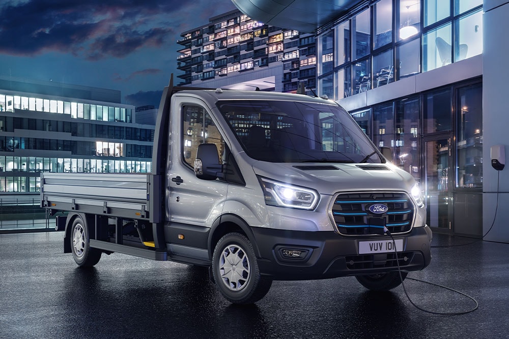 Una Ford Transit Chasis Cabina plateada estacionada frente a un edificio moderno por la noche.