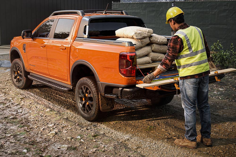 Un trabajador de la construcción cargando equipos de trabajo en la plataforma de una Ford Ranger naranja.