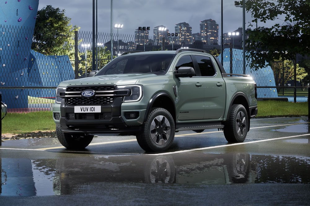 Una Ford Ranger híbrida enchufable gris aparcada frente a un paisaje urbano al atardecer.