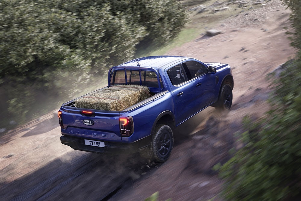 Vista trasera desde arriba de una Ford Ranger  azul circulando por un camino de tierra.