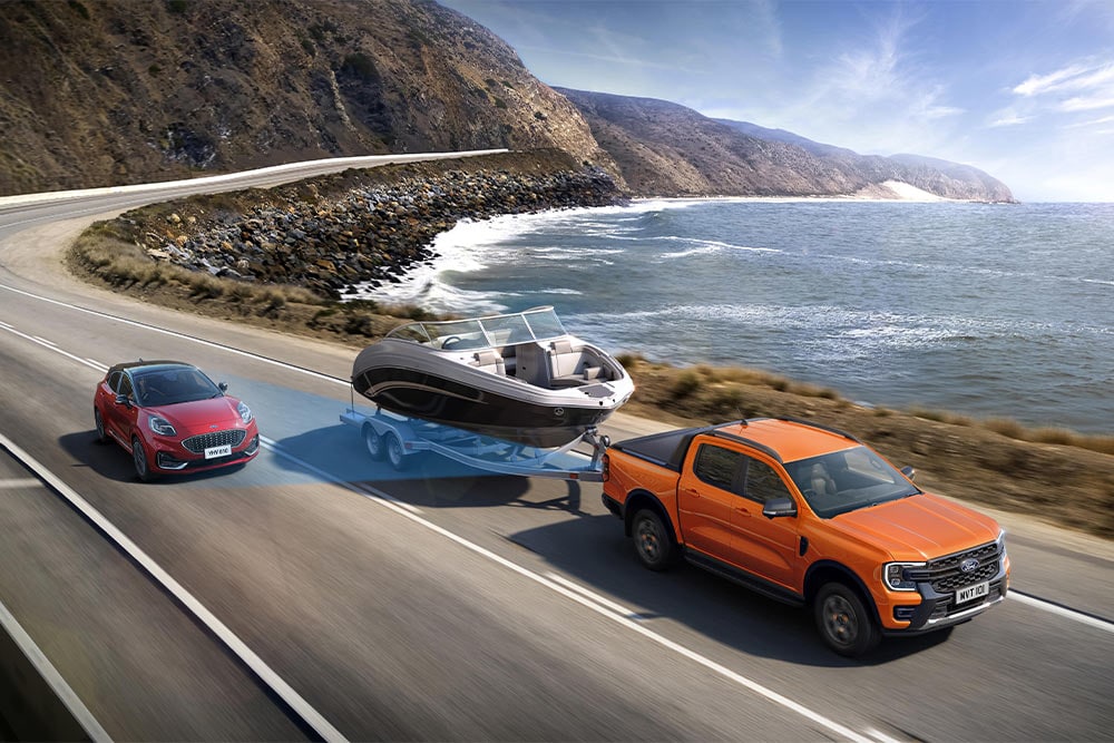 Una Ford Ranger naranja remolca un barco mientras circula por una carretera de la costa, demostrando así su gran capacidad de remolque.