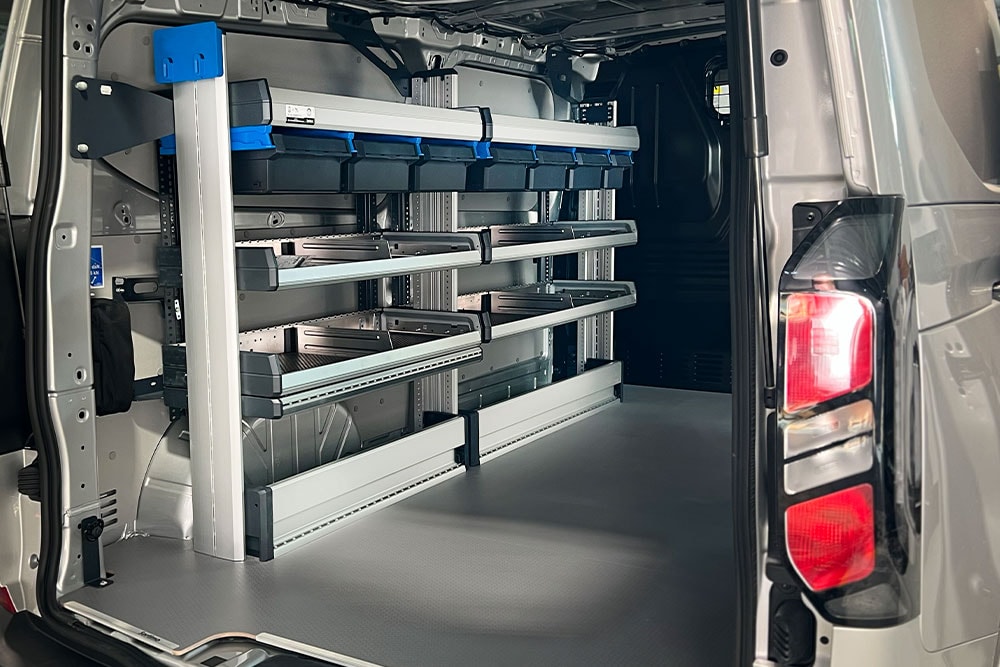  Interior trasero de una furgoneta Ford Transit, mostrando un sistema de estanterías modular con varios contenedores de almacenamiento.