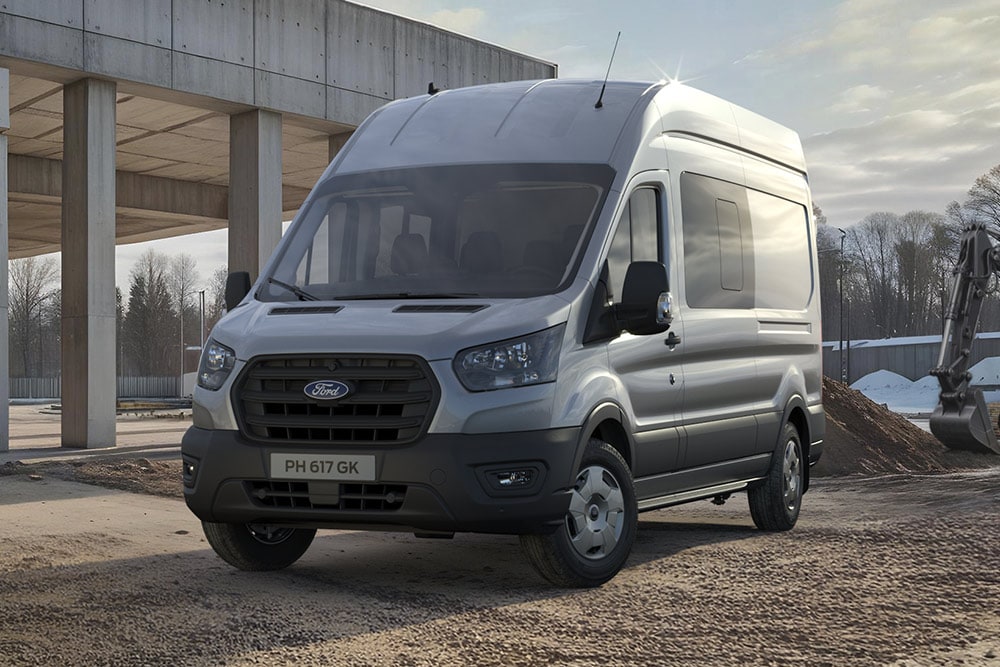 Ford Pro Transit plateado aparcado en una obra, con trabajadores de la construcción al fondo.
