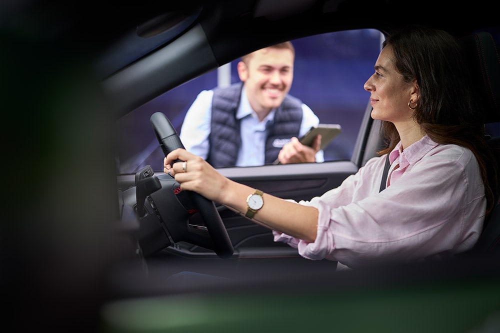 Una persona en el asiento del conductor de un vehículo Ford mira a un técnico que sostiene una tablet fuera del coche.