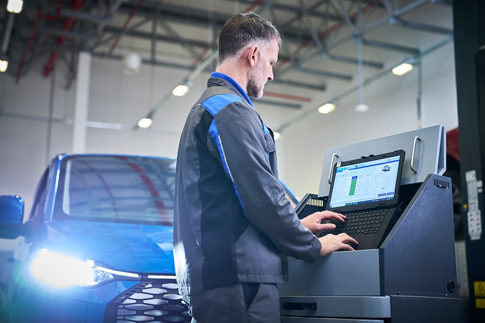 Un técnico trabajando en un portátil conectado a un SUV Ford azul en un puesto de mantenimiento.