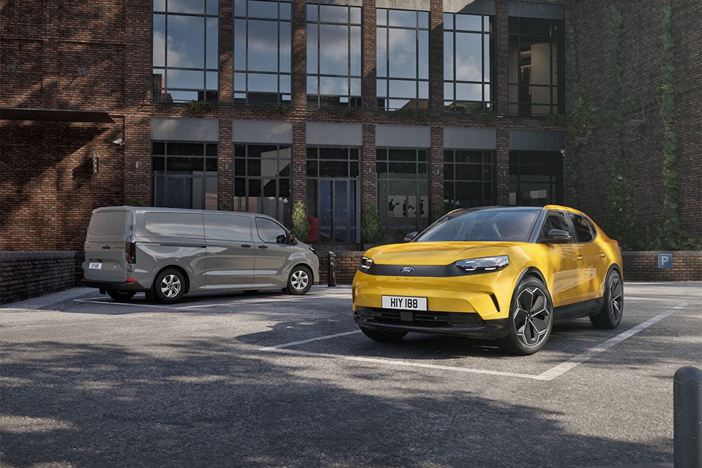  Una furgoneta Ford gris y un Ford Capri amarillo estacionados frente a un moderno edificio de ladrillo.