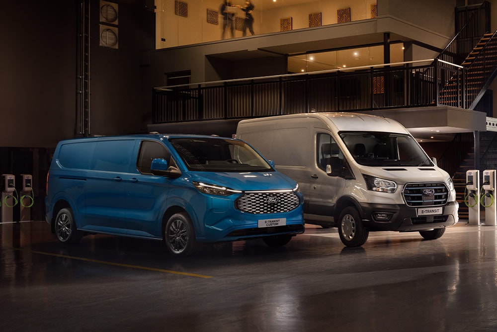 Una Ford E-Transit Custom azul y una Ford E-Transit plateada cargando en un aparcamiento.