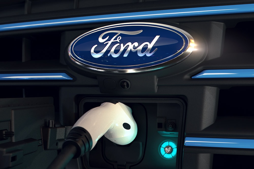Primer plano de un cable de carga blanco conectado a un puerto de carga delantero de un vehículo eléctrico Ford.