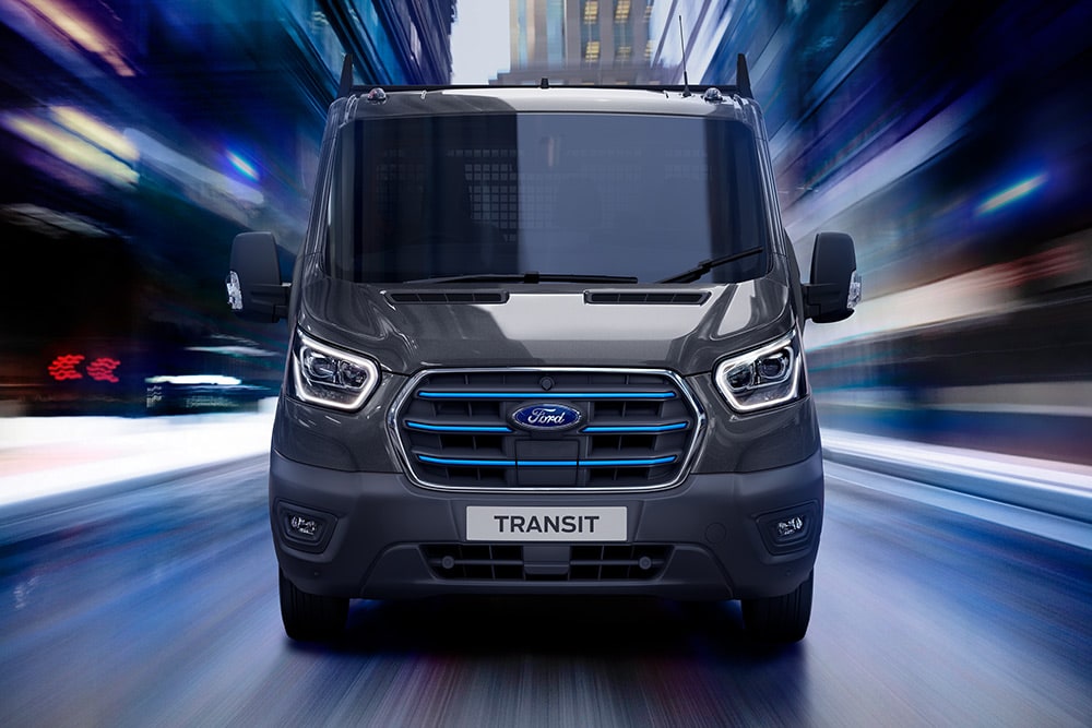 Ford Pro Transit plateado aparcado en una obra, con trabajadores de la construcción al fondo.